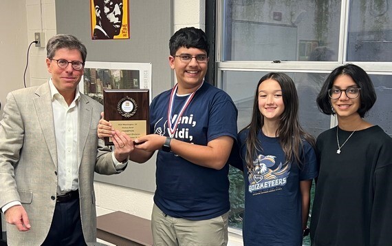 Middle School students and teacher standing together holding plaque