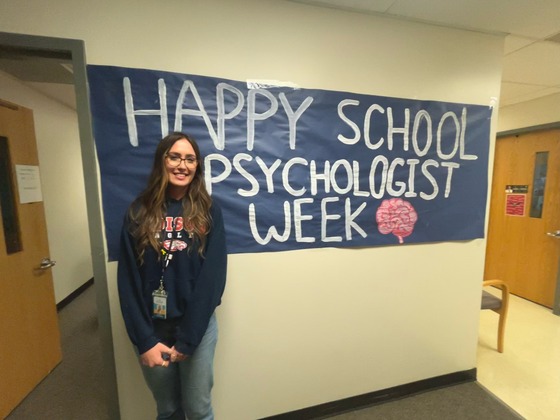 A woman standing in front of a sign that says Happy School Psychologist Week