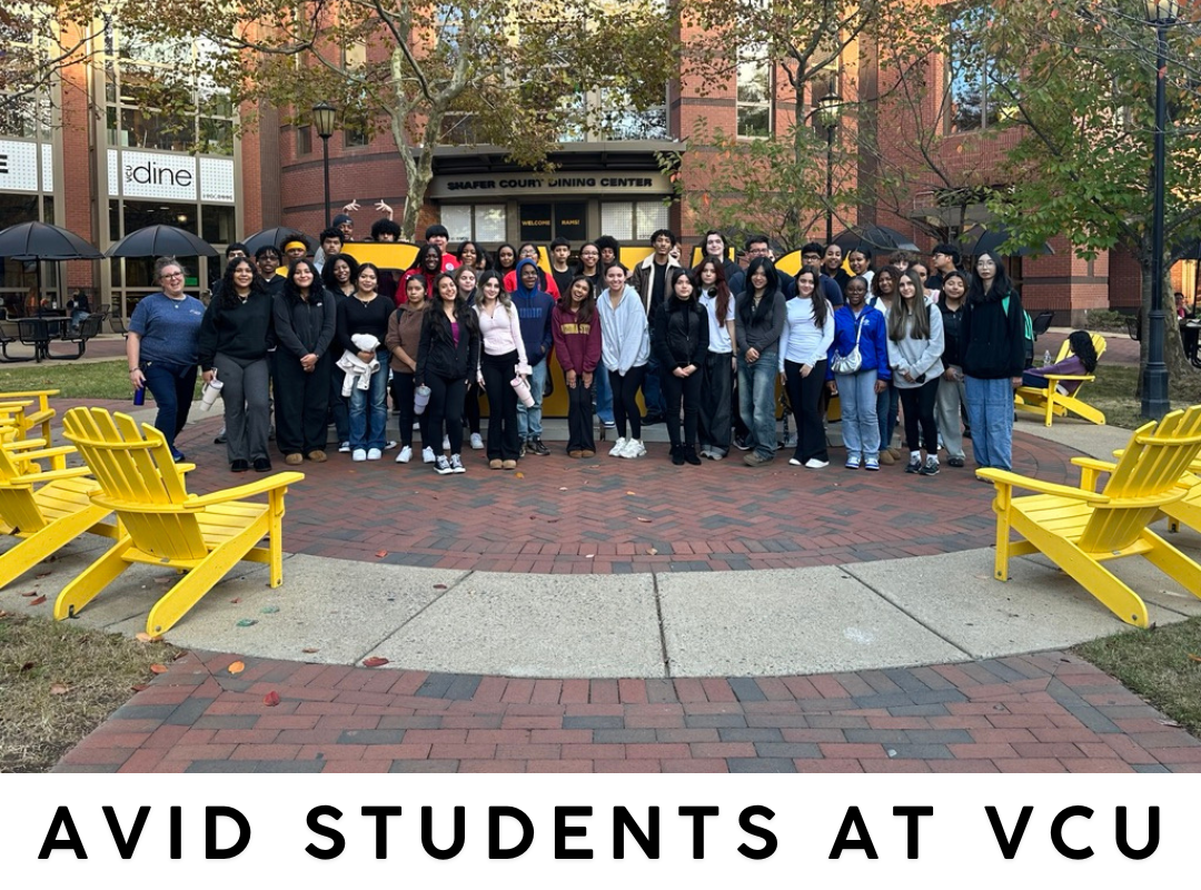 many students standing outside in a courtyard, 2 yellow chairs on either side of the group