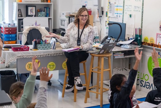 teacher sitting on a chair smiling and teaching in front of a classroom