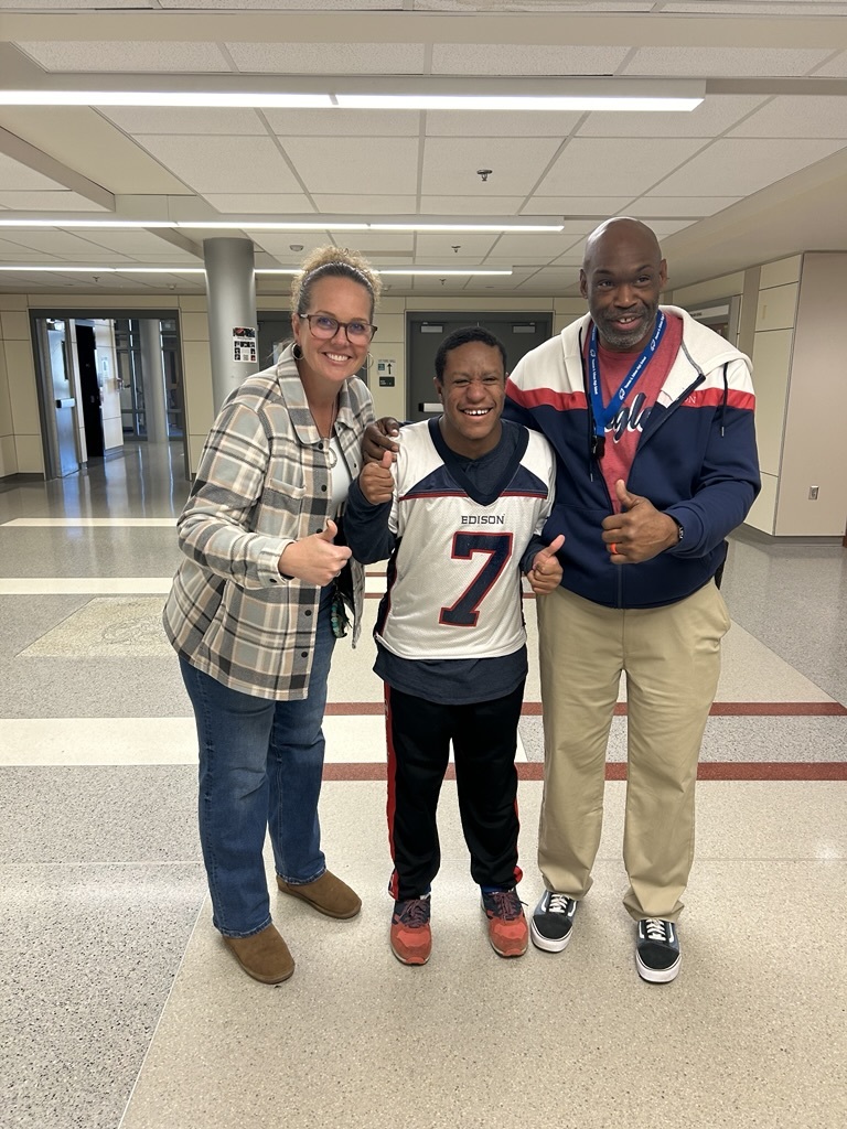 2 adults posing with a student between them, all have thumbs up!