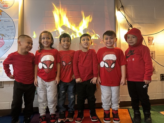 Six students dressed alike standing in front of a Yule Log video