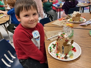 A boy smiles with his gingerbread house 