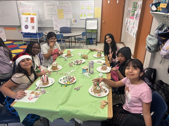 Students gather around the table to use food to make gingerbread houses 