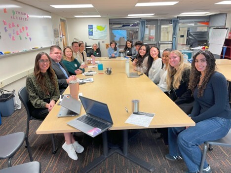 students and adults sitting at a long table smiling and looking at the camera