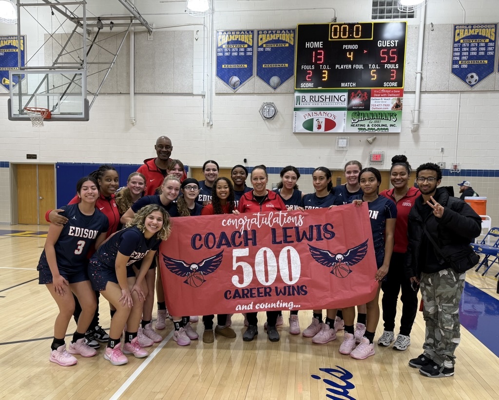 players and coach standing on the basketball court behind a sign that says congratulations coach lewis 500 career wins