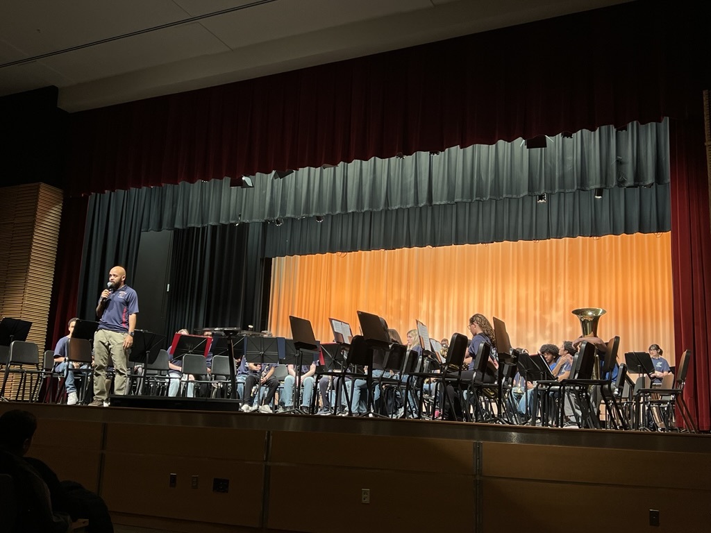 band director standing on stage with band students sitting onstage