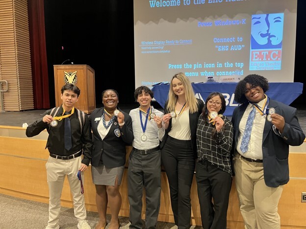 6 students standing in front of a stage holding medals