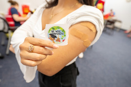 a woman with bandages on her arm where she was given immunizations holding a sticker that says be wise immunize