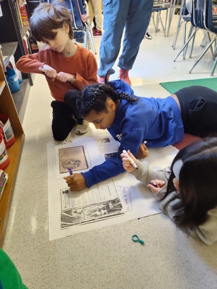 Students sit around a piece of chart paper and write on it 