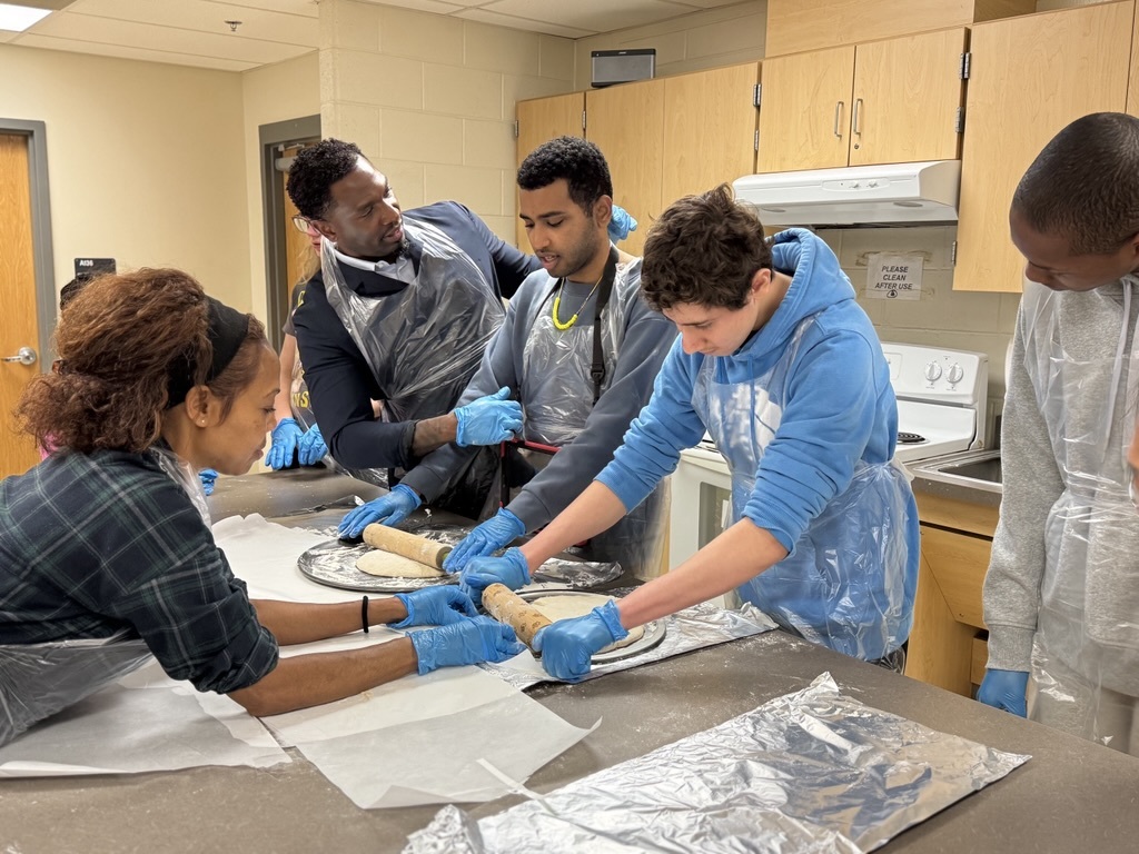 2 adults helping 3 students roll out pizza dough