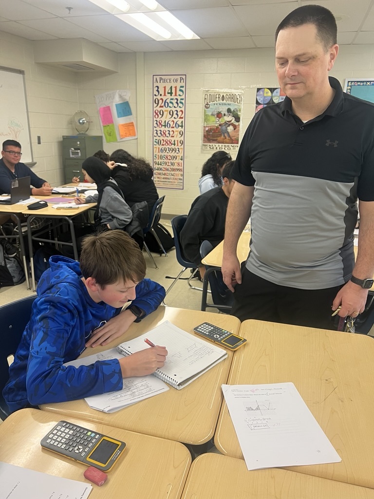 a teacher standing by the desk of a student 
