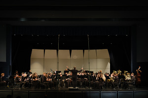 A symphonic band performs on stage with a conductor leading them.