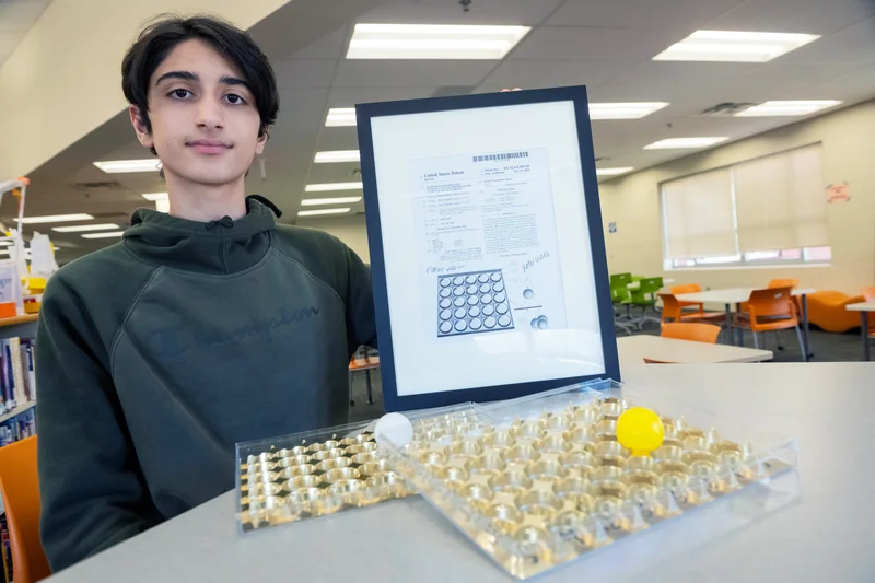 student smiles next to the math game he created