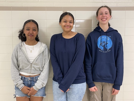 3 students standing in front of a wall smiling