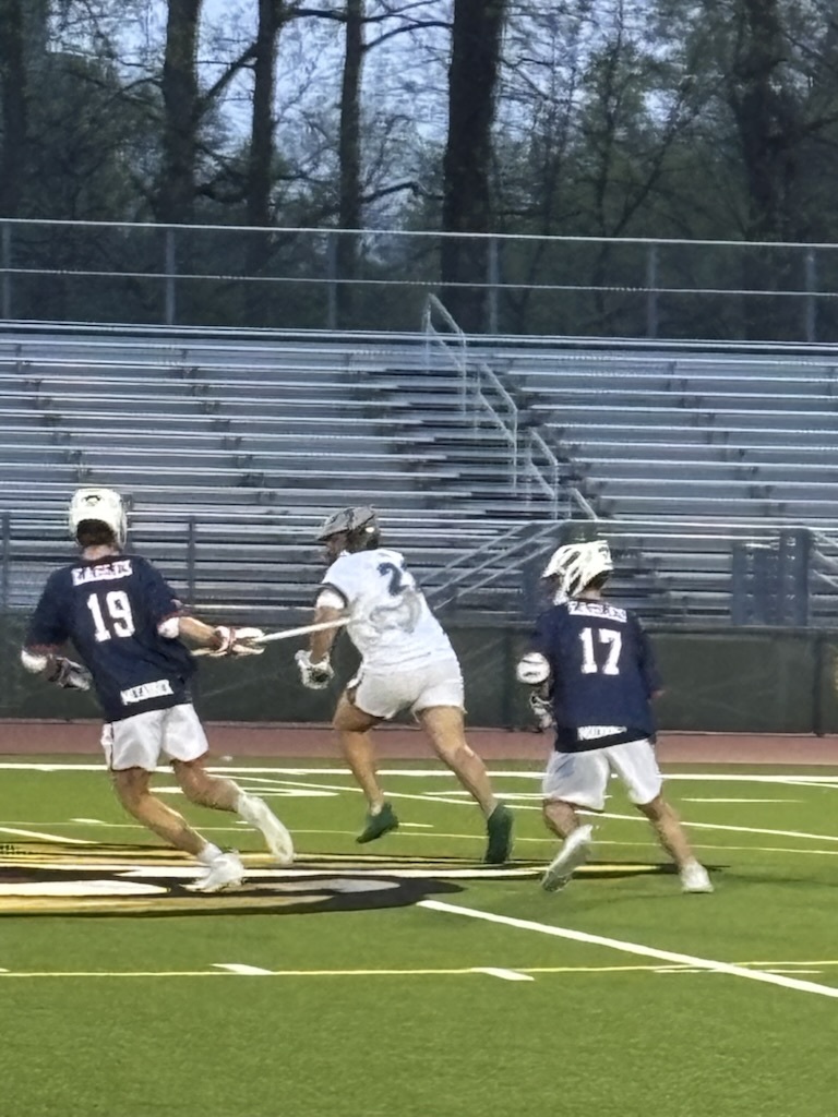 lacrosse players on the field, 2 with blue shirts and 1 with white