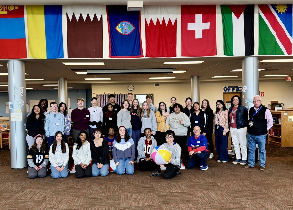 students standing in a room with flags coming down from the ceiling above them