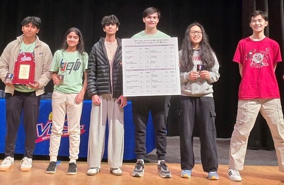 Students standing together on stage holding trophy