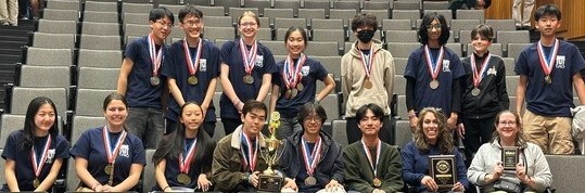 Students seated and standing in auditorium with medals hanging around their necks