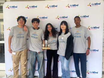 Five people in matching gray "McSolar" T-shirts stand together holding a trophy in front of a "KidWind Challenge" backdrop.