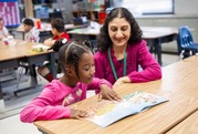 teachers sits with student at a desk and reads
