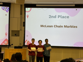 Three individuals holding certificates stand in front of a screen displaying "2nd Place McLean Chain Marbles."