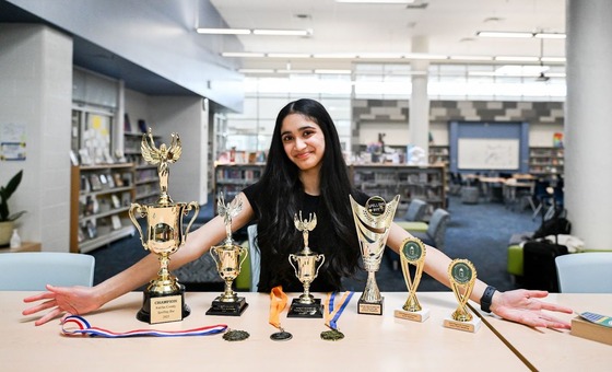 student showing off her many trophies inside of a library