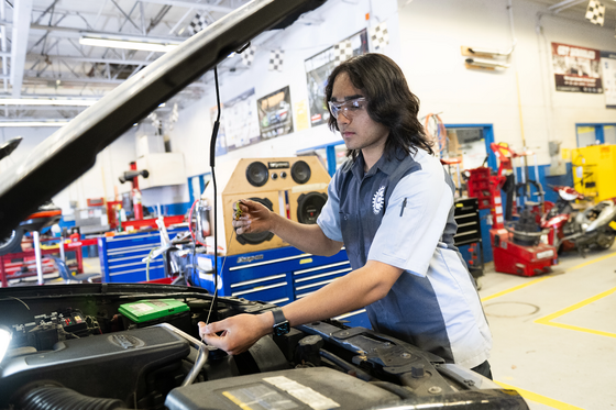 student in auto shop working under the hood of a vehicle