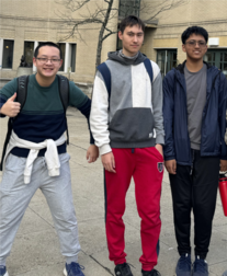 Three people standing outdoors with a building and tree in the background.