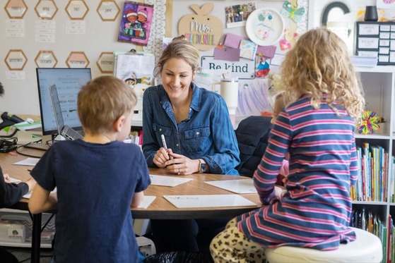 teacher smiling with students while they work on a worksheet while seated at a round table
