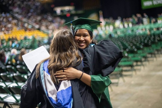 graduate in cap and gown hugs teacher during graduation