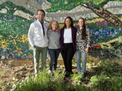 Mr. Hill, Ms. Carpenter, Ms. Curtis, and Ms. Theiss stand in front of the courtyard mural