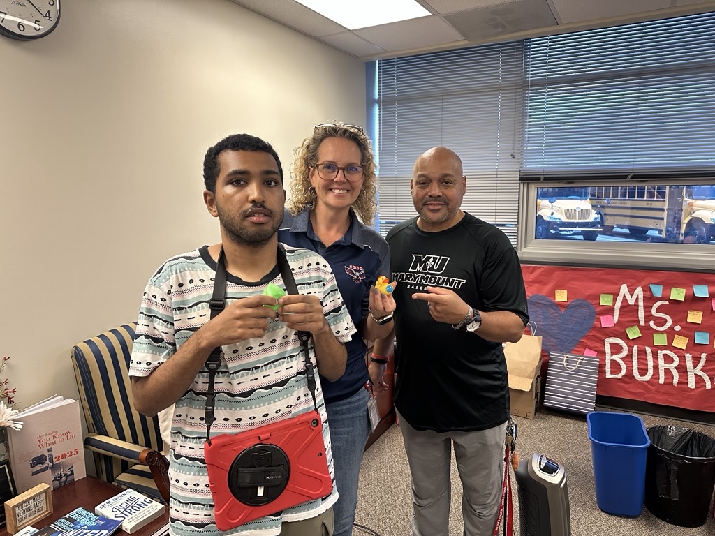 3 people standing in an office, 2 are holding small toy ducks