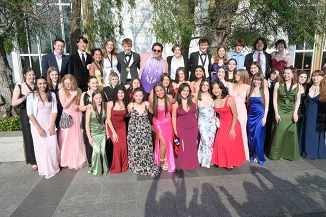 A large group of young people in formal attire posing together outdoors.