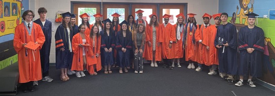 Class of 2025 graduates posing the main lobby of their old school with Mrs. Schadle