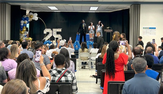 Administrators preparing to present certificates while 6th graders parade in