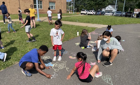 5th graders and kindergarten students playing with sidewalk chalk