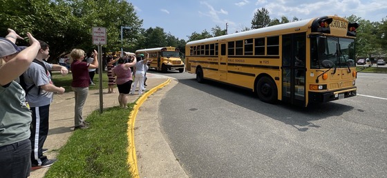 Staff members waving to students in the buses as they pull away