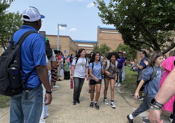Staff members waving and clapping as students leave the building and head to the buses