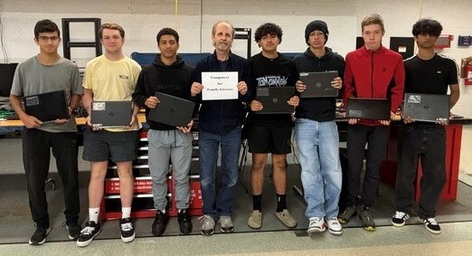 students and teacher standing in row holding laptops