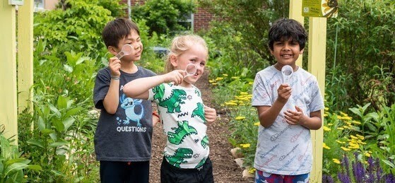 Children standing in garden holding magnifying glasses