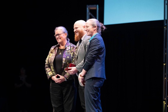 three employees smile on stage with a plaque award