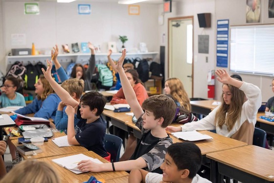 students in a classroom with their hands raised
