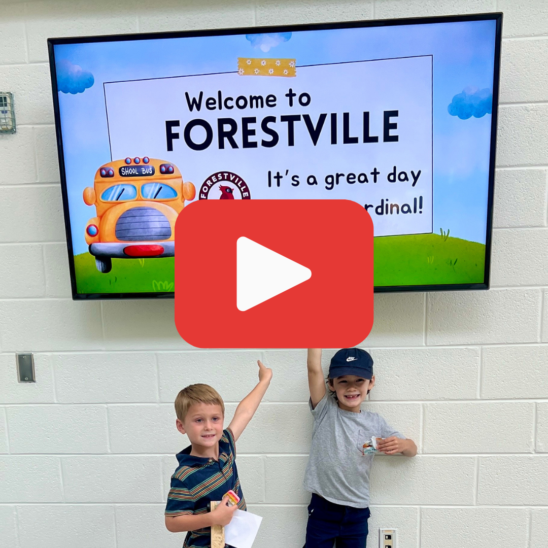 Twp students under a TV that says Welcome to Forestville with a bus.  A large red play button is overlayed on the photo