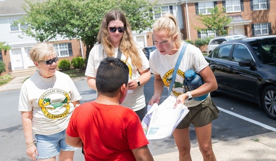 teachers saying hi to a student and giving him a packet of back to school materials