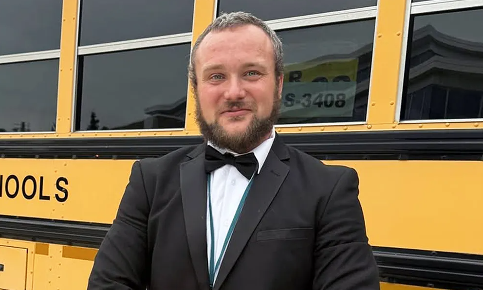 A man in a tux stands in front of a school bus.