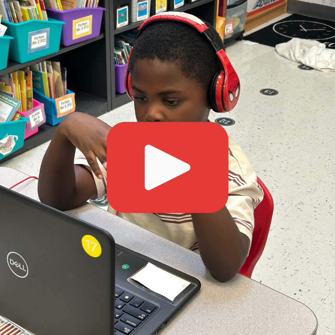 A student sitting at a laptop with headphones on. A red Play button overlayed on the photo