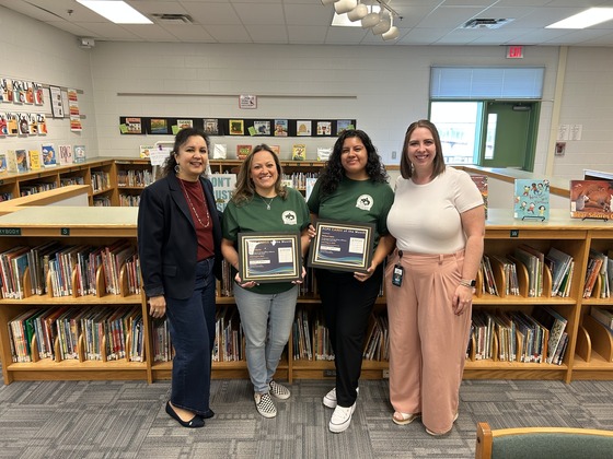Four women stand with two holding a reward 