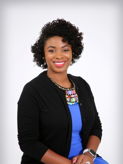 Person smiling in a blue dress and black cardigan with a colorful necklace.