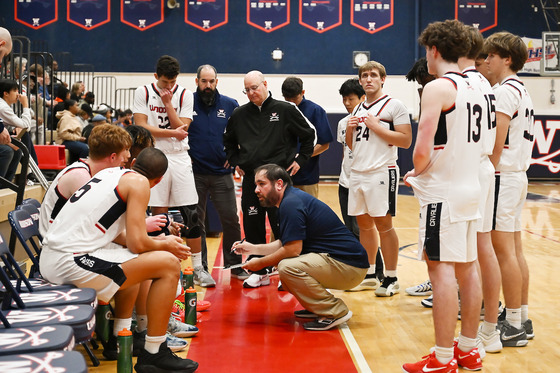 Coach kneels as he talks to his team during a time out huddle
